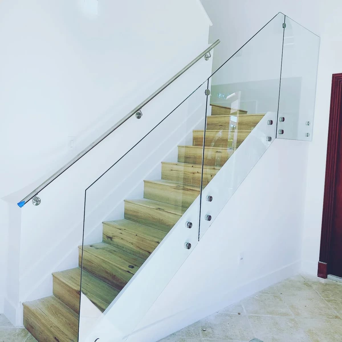 Glass stair railing with stainless steel handrail and standoff clamps on a wooden staircase