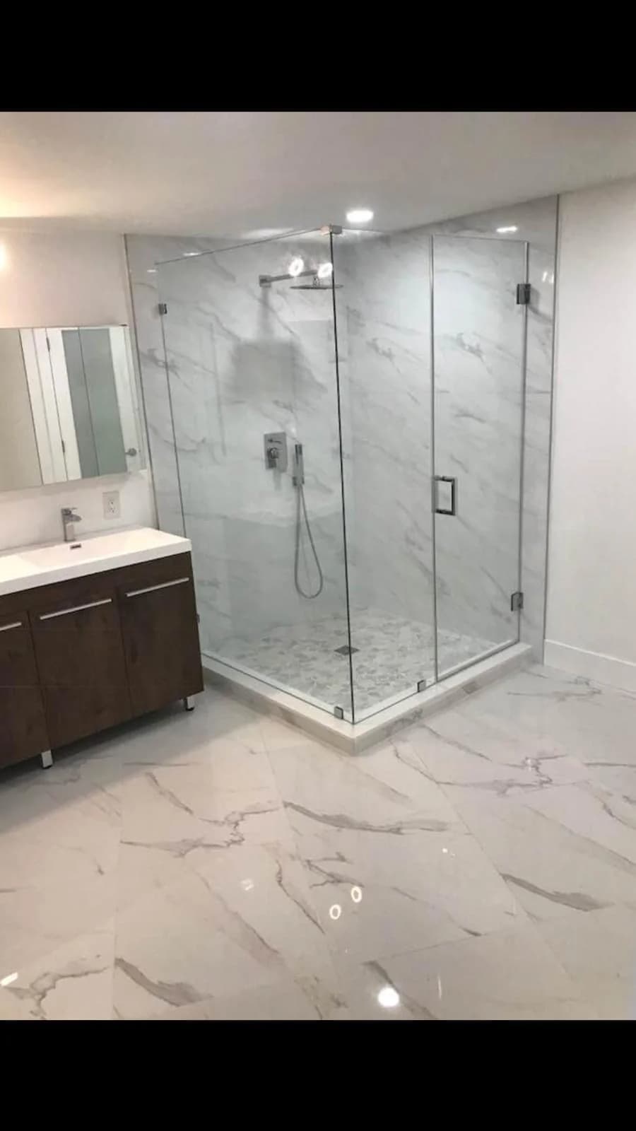 Frameless hinged glass shower door on a corner enclosure with a wide step-in opening