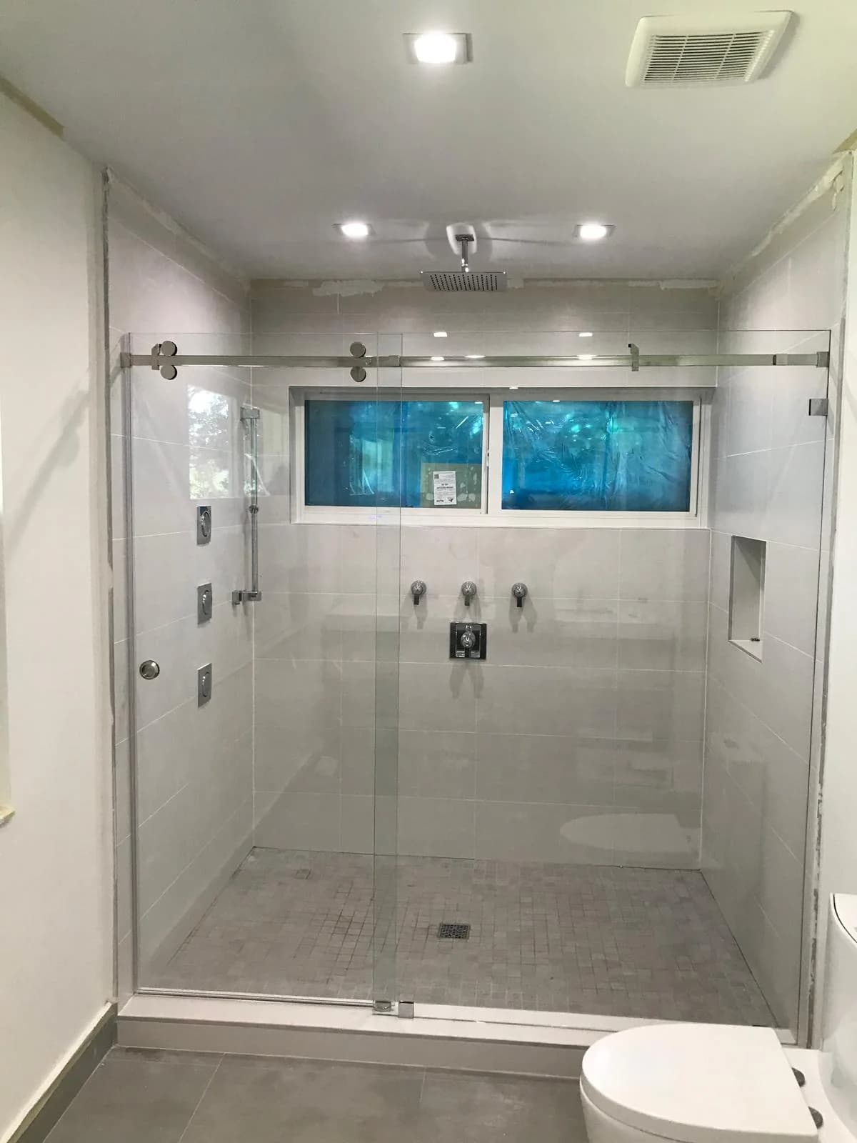 Frameless sliding shower door with exposed stainless rollers on a wide alcove shower