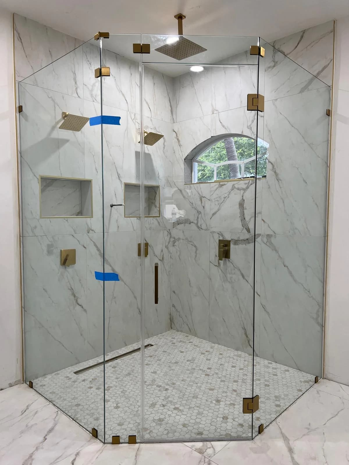 Frameless clear glass shower door with brushed gold hardware in a marble bathroom
