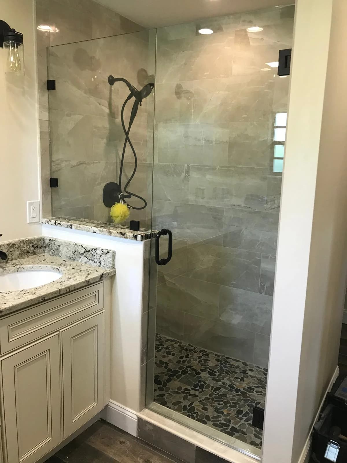 Hinged frameless shower door with black hardware next to a vanity