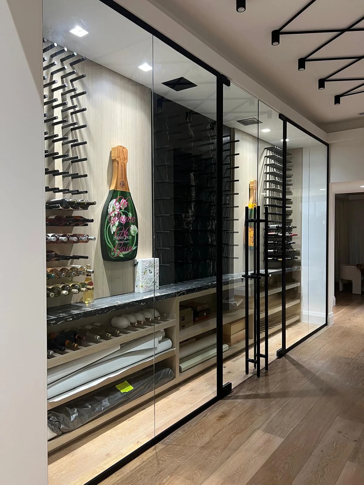 Glass-enclosed wine room with black frames and wall-mounted bottle racks