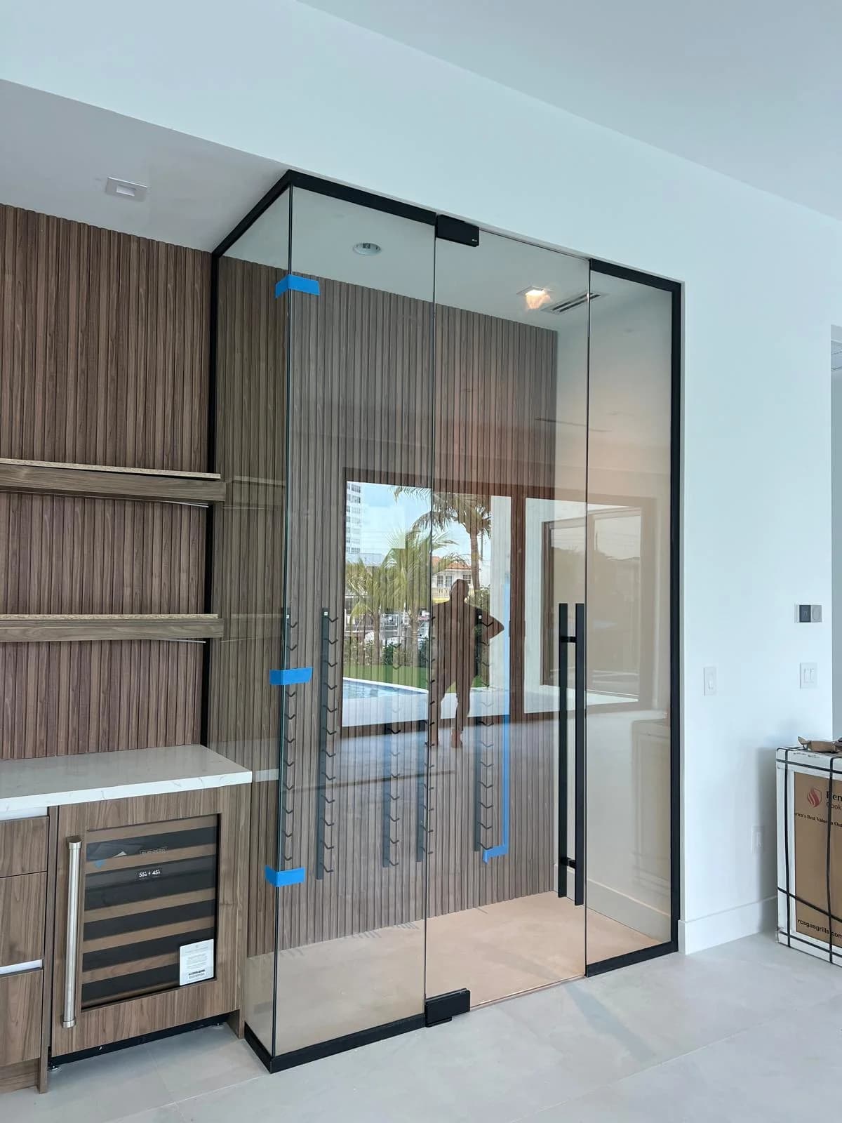Glass wine room enclosure with sealed glass door next to a wet bar